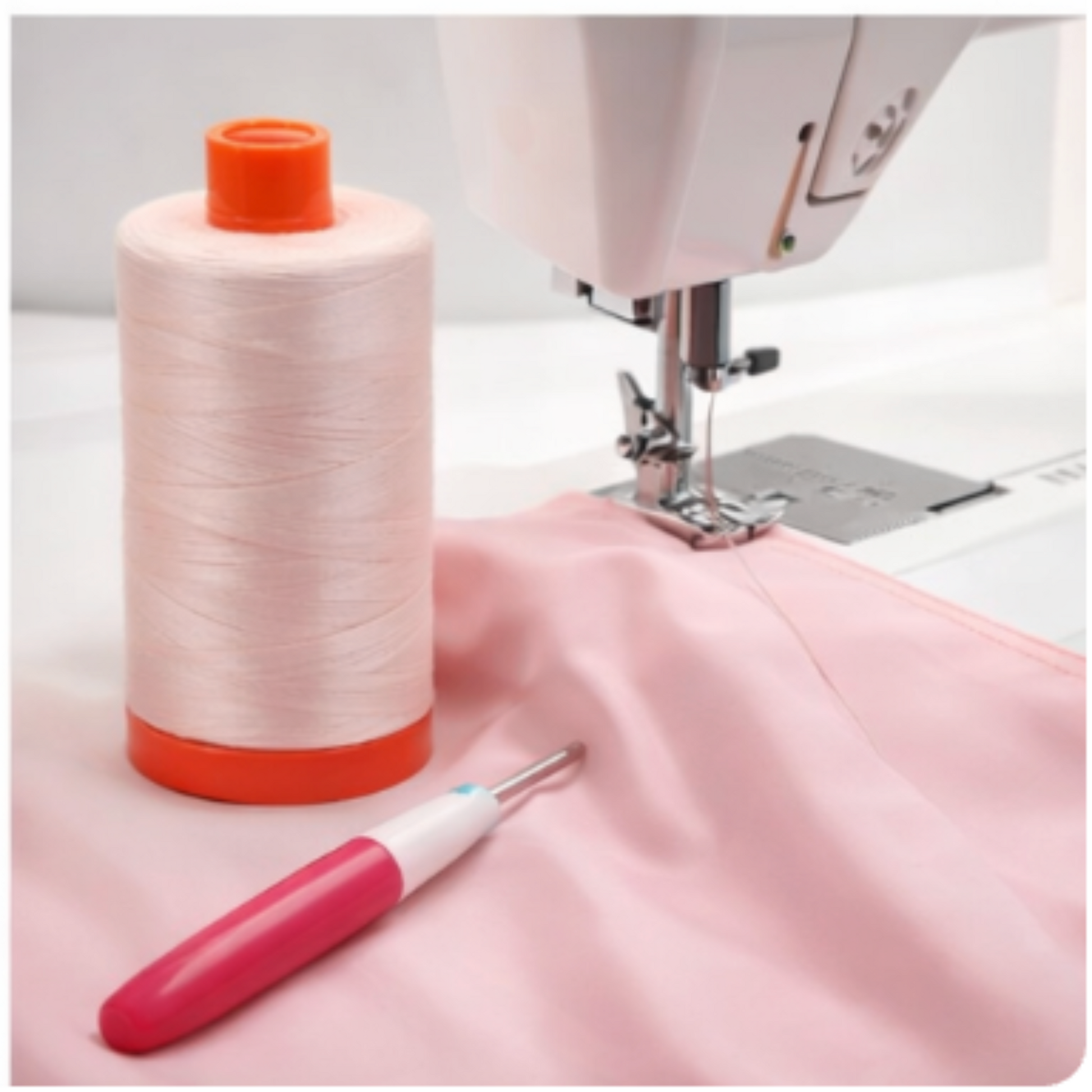Aurifil Mako Cotton Thread 50wt Light Sand beside sewing machine on soft pink fabric