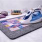 Ironing a colorful quilt on a gray pressing wool mat with an iron.