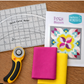 Quick Curve Ruler on a wooden table with rotary cutter and bright quilting fabrics, showing curved cutting setup.