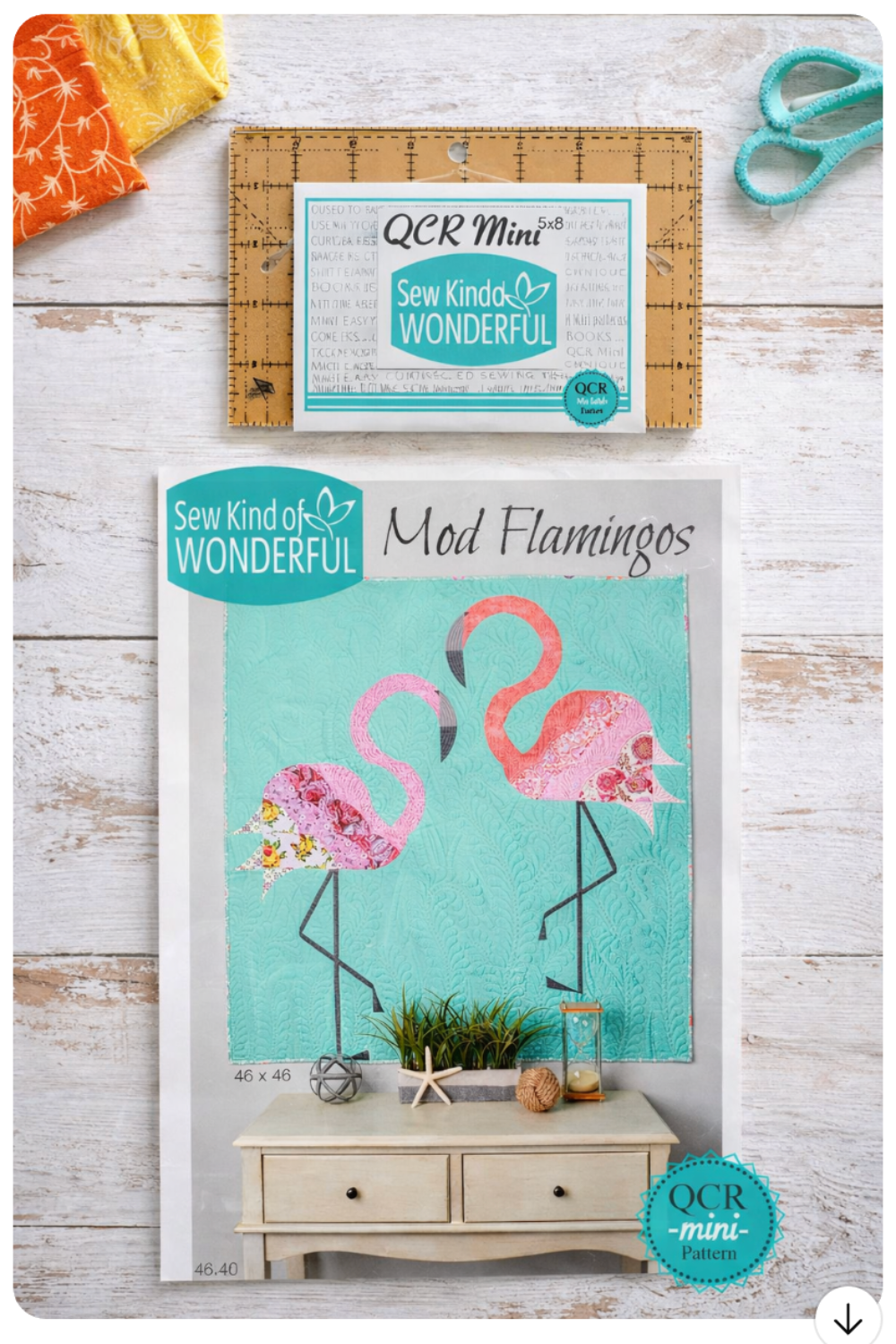 Casual flat-lay photo of the Sew Kind of Wonderful QCR Mini ruler and Mod Flamingos quilt pattern on a light wood surface with scissors and fabric accents.