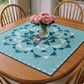 Town Square Garden quilt table topper in blue tones used as a 35 inch square centerpiece on a wooden dining table
