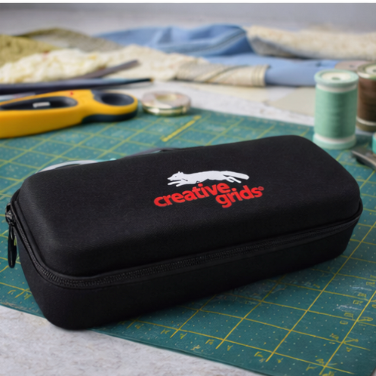 Black case with 'creative grids' logo on a cutting mat with sewing tools.