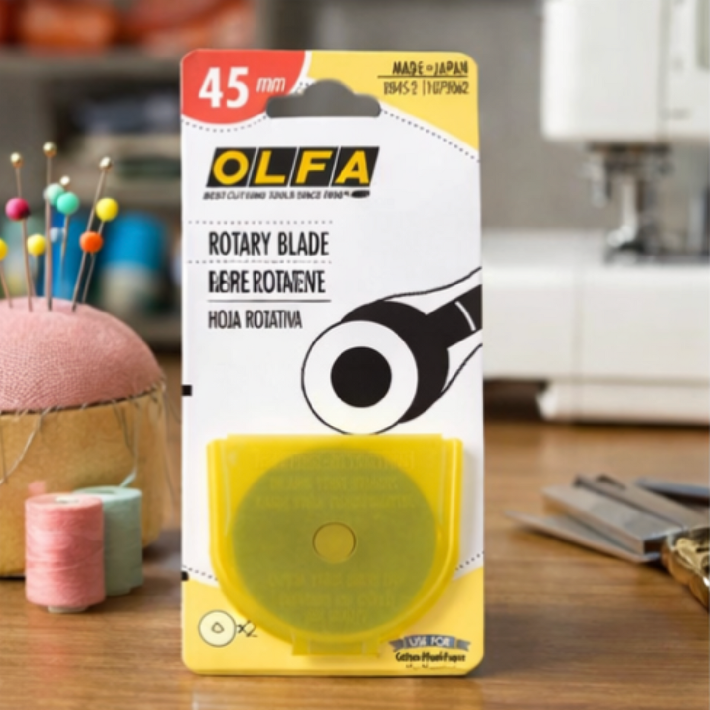 OLFA 45mm rotary cutter replacement blades packaging in sewing room with thread spools and pincushion