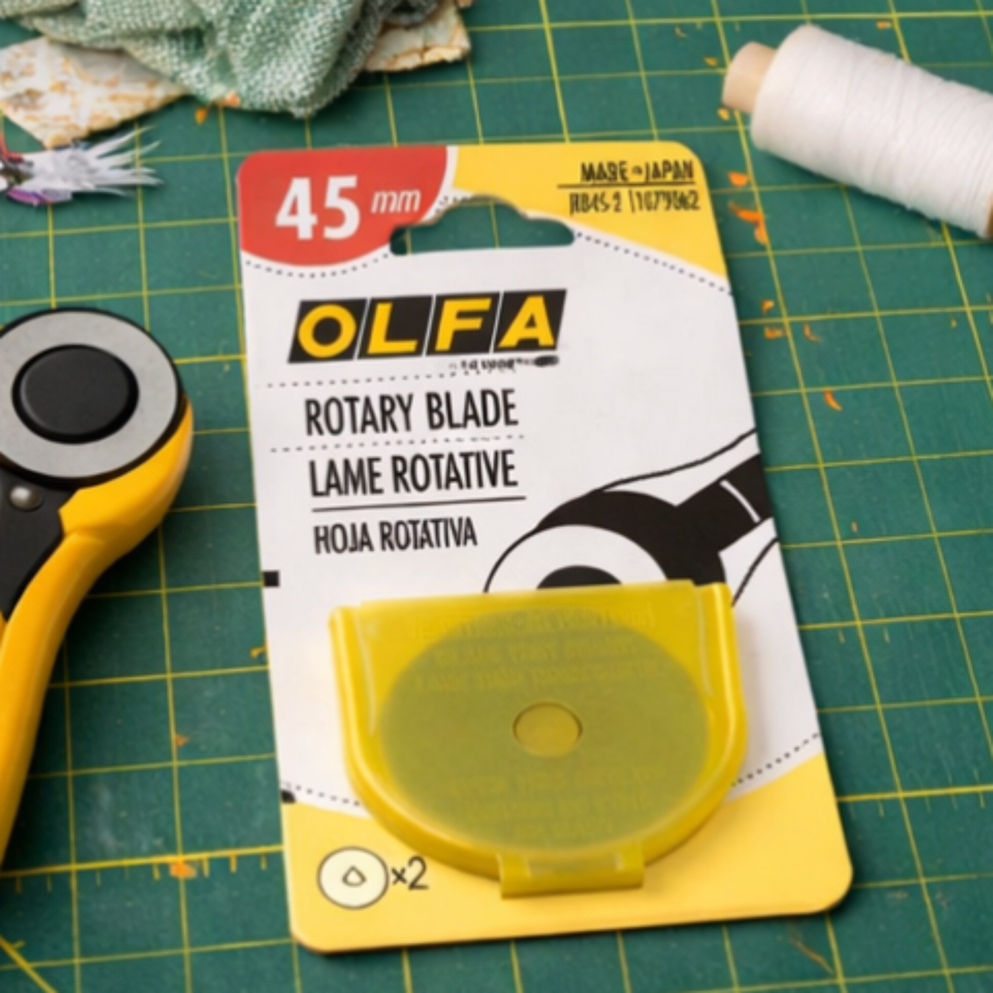 OLFA 45mm rotary blade pack placed on green cutting mat next to rotary cutter in quilting workspace