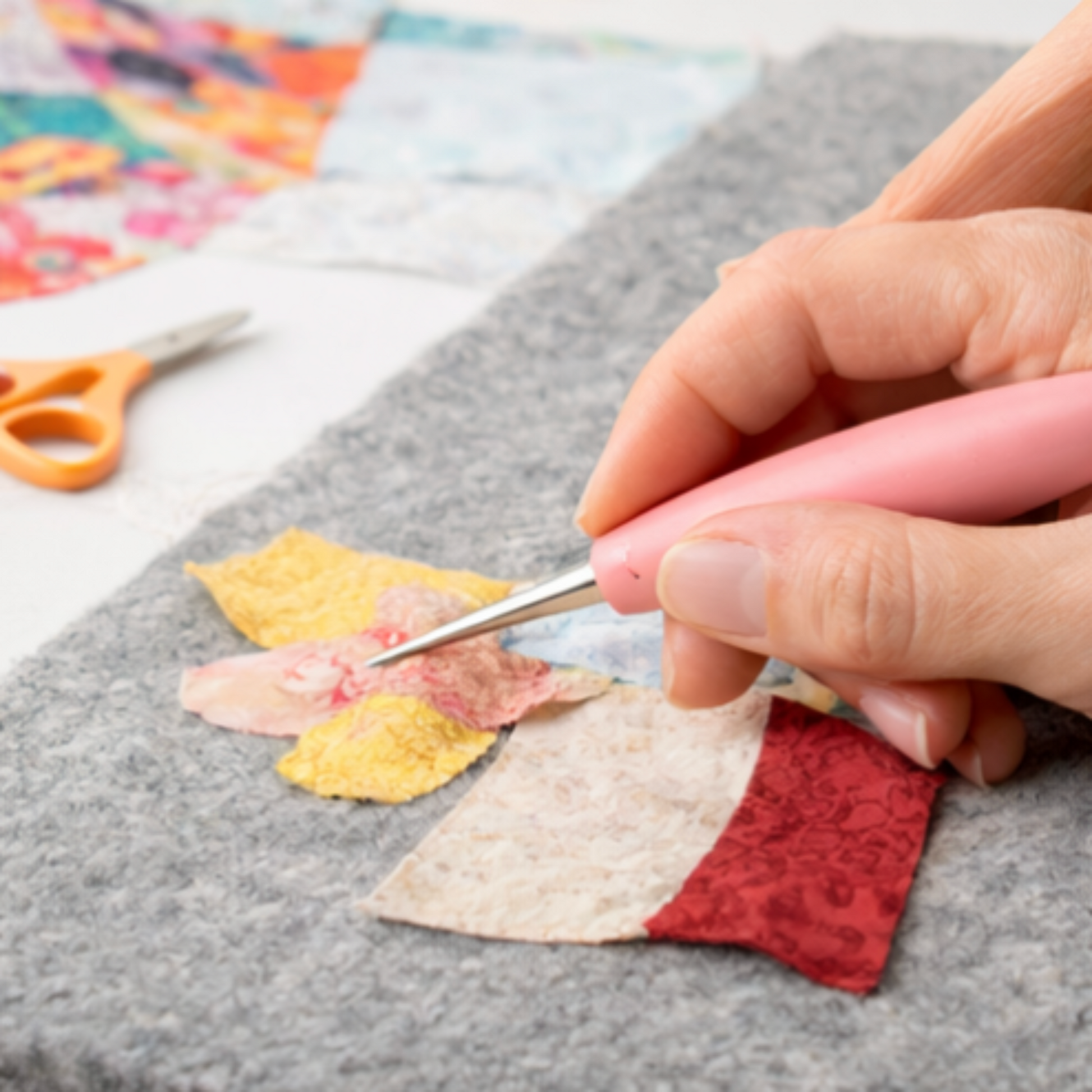 Pink handled quilting stiletto positioning small fabric pieces during appliqué quilting work on felt surface.