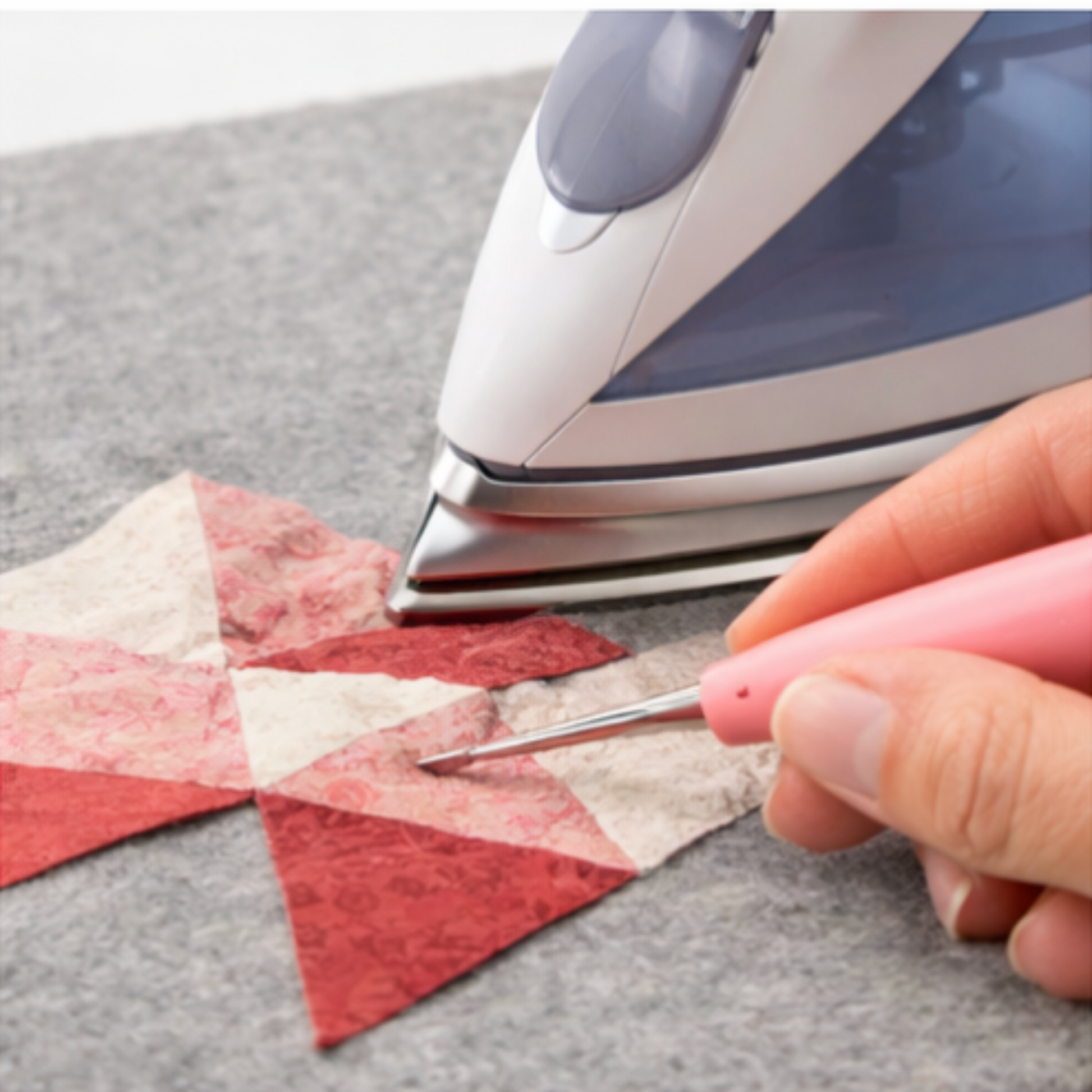 Stiletto assisting seam placement while pressing quilt block with iron during patchwork sewing.