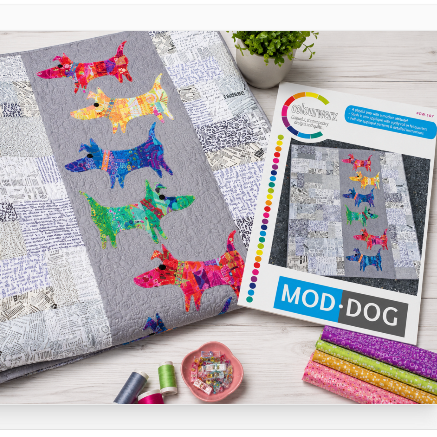 ModDog quilt pattern and finished applique dog quilt displayed with colorful quilting fabrics and sewing supplies on crafting table