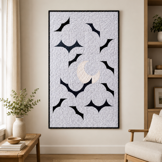 Modern moon and bat wall quilt hanging in a neutral living room above a wooden side table and beside a cozy cha