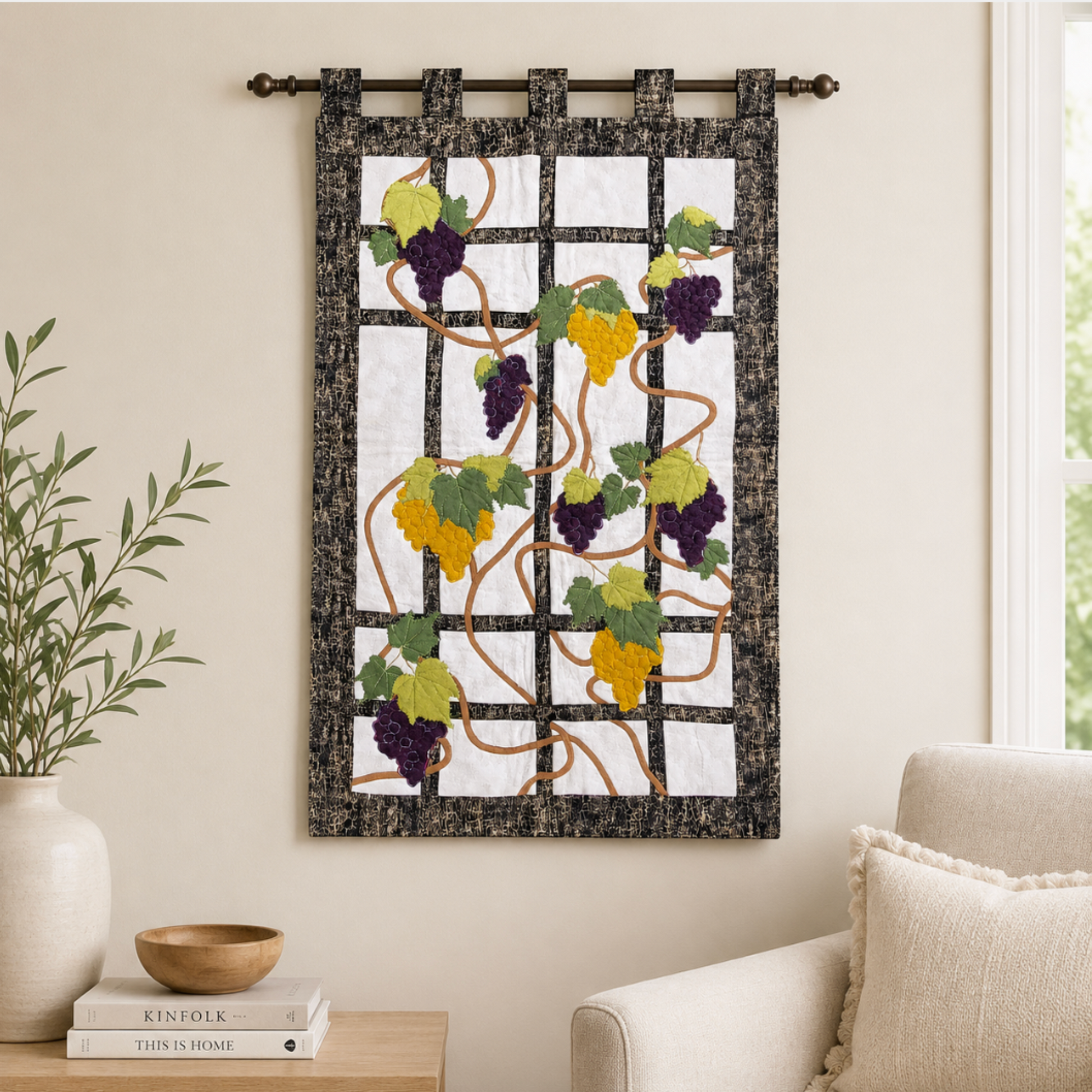 Handmade grapevine quilt wall hanging displayed in a neutral living room with purple and golden grape clusters on a black trellis design.