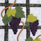 Close-up of grapevine quilt wall hanging showing purple grape clusters, green leaves, and black trellis appliqué detail.