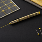 Yellow Pigma Micron 08 fabric marking pen drawing a fine yellow line on dark fabric beside a quilting ruler and sewing pins, ideal for quilting and sewing projects.