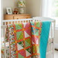 Handmade In the Jungle quilt draped over a white crib in a bright nursery, showing colorful jungle animal prints and turquoise backing.