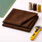 Interwoven Brown by Jason Yenter – lifestyle shot with folded fabric, spools of thread, rotary cutter and cutting mat, clean minimal setting