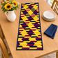Golden Weave quilted table runner on a wood dining table beside a white pitcher of sunflowers, stacked cream plates and a folded navy napkin.