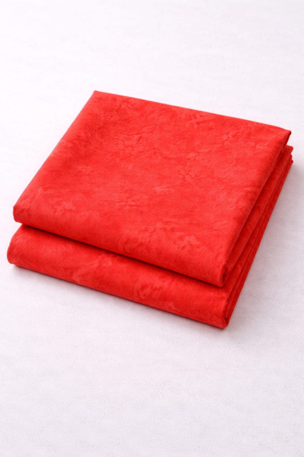 Expressions Batiks Hand-Dyes Tomato Red fabric by Riley Blake Designs folded in two neat stacked pieces on a white surface – bold vivid tomato red tonal hand-dyed batik with subtle lighter rose highlights and deeper crimson organic mottled variation, a striking warm focal blender perfect for warm-toned, patriotic, and holiday quilts, 100% cotton batik