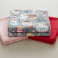 Alice Multi Teacups fabric by Jason Yenter for In The Beginning Fabrics folded on a light linen surface with coordinating pink and red fabrics – whimsical Mad Hatter tea party scatter print with teacups, saucers, hearts, and lace on soft grey, perfect for children's quilts and novelty projects, 100% cotton, 3 yard cut