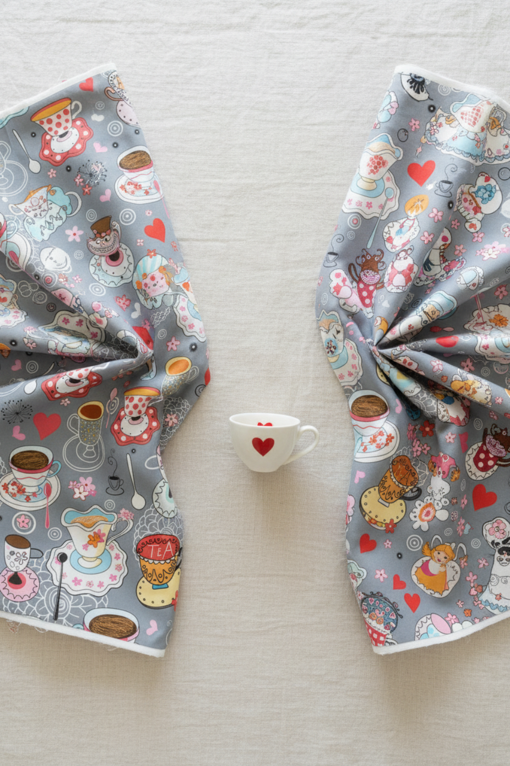 Alice Multi Teacups and Alice Multi Characters quilting cotton fabrics by Jason Yenter for In The Beginning Fabrics shown together – whimsical Mad Hatter tea party teacups and Alice in Wonderland character scatter prints on soft grey, perfect for children's quilts and novelty projects, 100% cotton, 3 yard cut