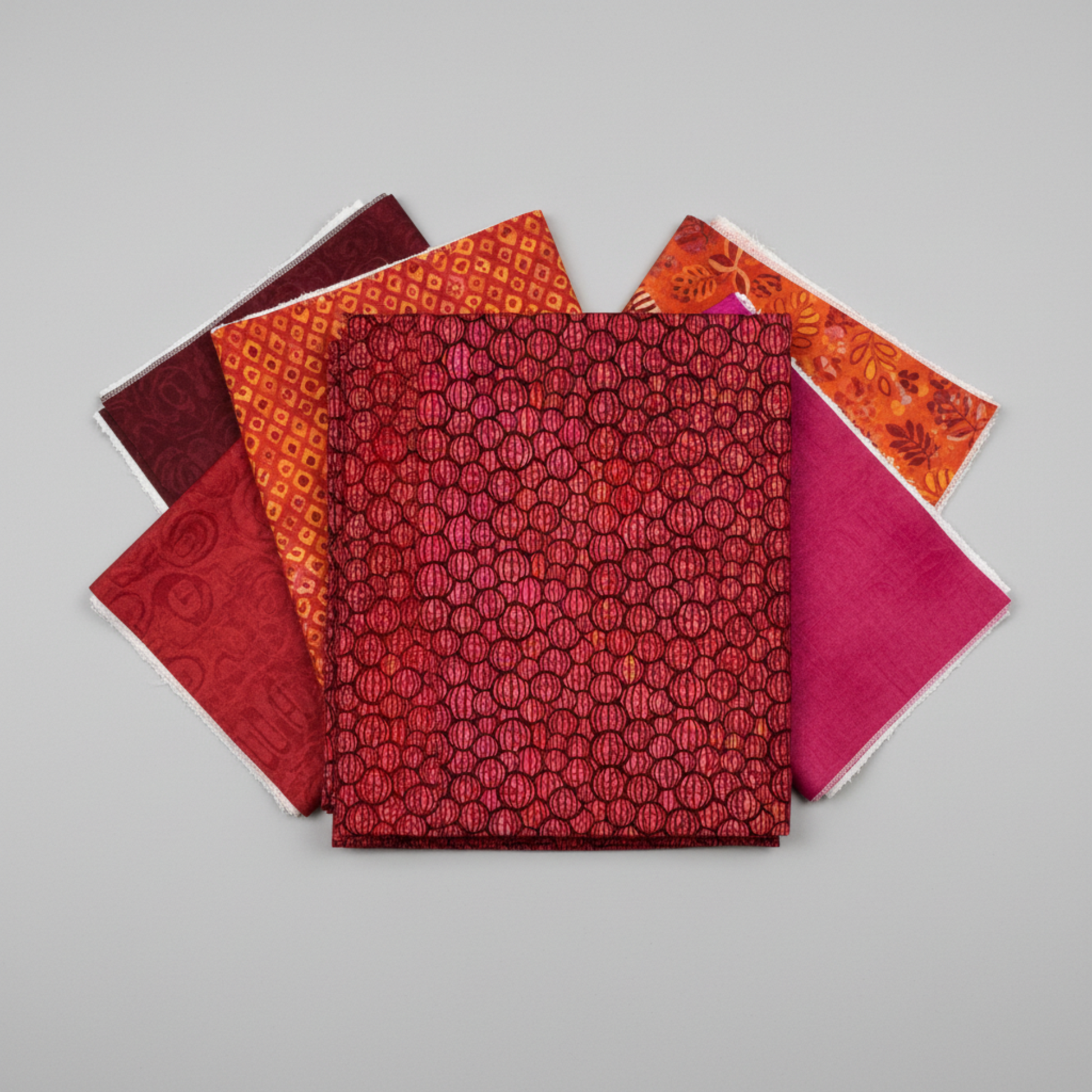 Allure Red Lanterns quilting cotton fabric by Jason Yenter for In The Beginning Fabrics shown in a coordinate stack with complementary warm-toned quilting fabrics in deep burgundy, crimson, magenta, and orange – allover striped oval lantern pattern, 100% cotton, 3 yard cut
