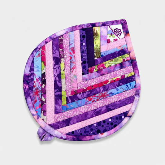 Leaf-Shaped Quilted Hot Pad – Violet Bloom, front view showing herringbone chevron strip piecing in deep violet, purple, lavender, pink, magenta, blue, and chartreuse prints with soft pink binding border and floral accent – handmade by IraRobi Quilts
