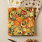 Autumn Celebration Multi Vegetables quilting cotton — vertical flat lay as hero fanned with coordinating autumn fabrics, brass scissors, and amber thread spools on a warm cream linen surface. Coordinating fabrics and quilt patterns available at IraRobi Quilts.