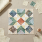 Quilting work-in-progress flat lay showing a Barn Star quilt block with Expressions Batiks Breathe Laurel fabric by Riley Blake Designs as the cream background – cream and ivory tonal batik with feathery fronds and leaf sprigs in soft sage green and taupe, with coordinating sage green, teal, and brown tonal batik star points and accent diamonds, loose cut fabric pieces, cream thread spool, and silver thimble on a warm linen surface