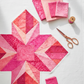 Modern quilt flat lay featuring Expressions Batiks Hand-Dyes Begonia by Riley Blake Designs as the focal fabric – pure saturated hot pink hand-dyed batik with organic painterly texture in pieced blocks with coordinating coral, magenta, and soft blush tonal batiks, with folded fabric swatches on a white linen surface