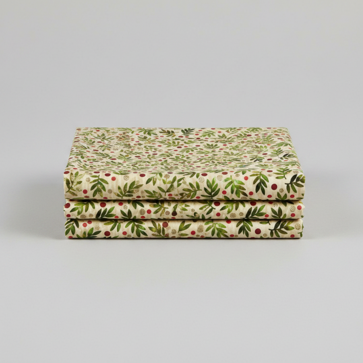 Winter Solstice II Beige Twigs Metallic quilting cotton by Jason Yenter for In The Beginning Fabrics — three folded yards stacked on a grey surface showing tossed watercolor green fern sprigs with red berry dots and gold metallic berry clusters on warm beige ground. Coordinating fabrics and quilt patterns are available at IraRobi Quilts.