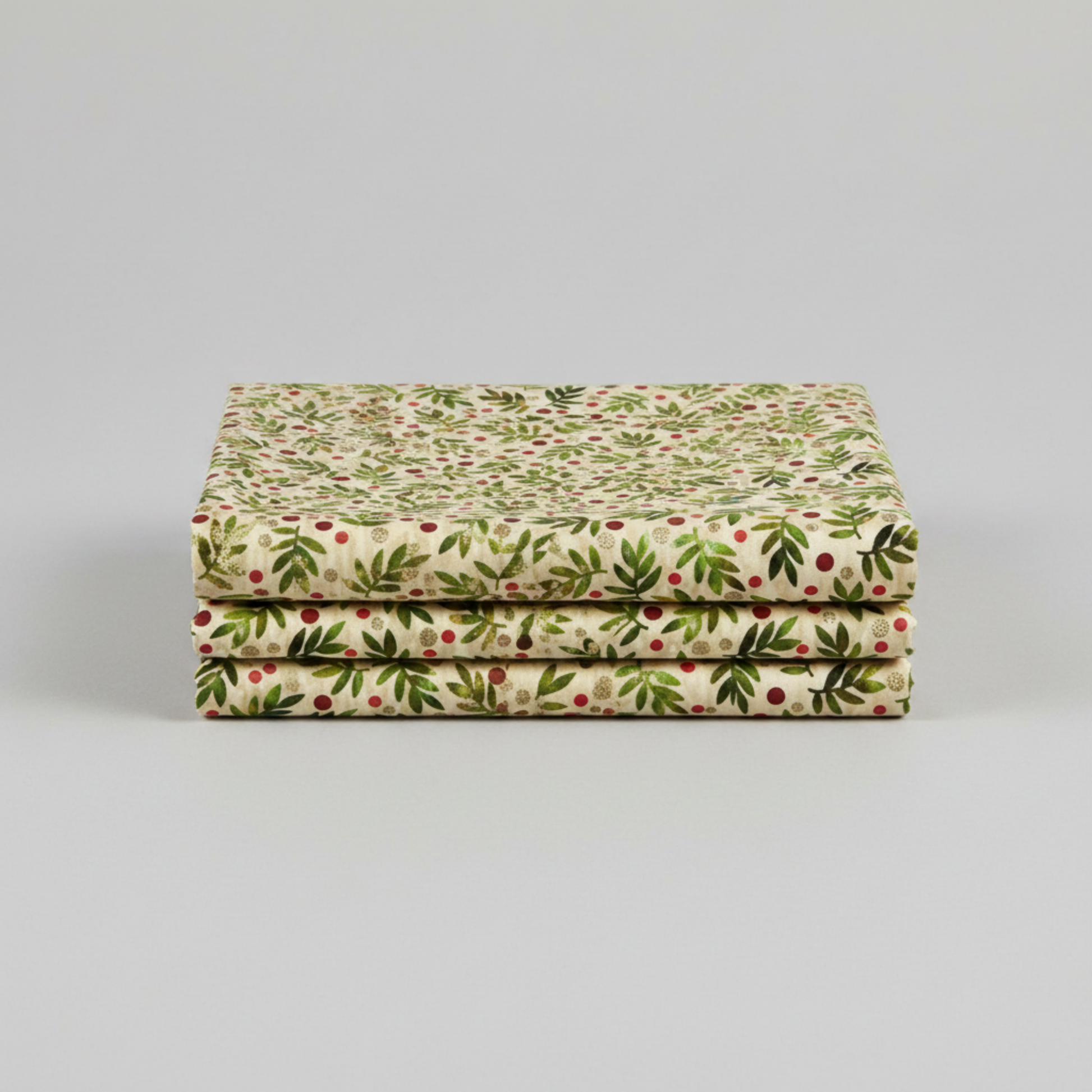 Winter Solstice II Beige Twigs Metallic quilting cotton by Jason Yenter for In The Beginning Fabrics — three folded yards stacked on a grey surface showing tossed watercolor green fern sprigs with red berry dots and gold metallic berry clusters on warm beige ground. Coordinating fabrics and quilt patterns are available at IraRobi Quilts.