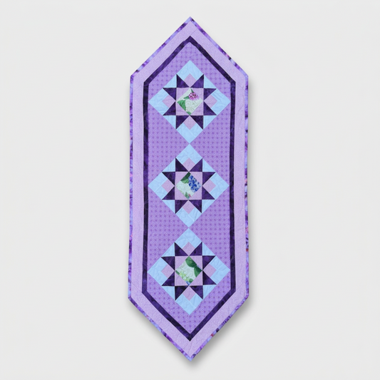 Bread and Butter Berry Patch quilted table runner with three purple star blocks, floral centers and lavender borders on light gray.