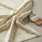 Expressions Batiks Breathe Laurel fabric by Riley Blake Designs draped on a warm linen surface with small folded coordinating sage green, cream, and taupe batik swatches nearby – cream and ivory tonal batik with feathery fronds and leaf sprigs, a sophisticated botanical blender perfect for nature-inspired and soft palette quilts, 100% cotton batik