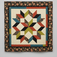 Scraps of Kindness Cream Nine Patch Boxes Fabric by Kim Diehl for Henry Glass — vertical view of the Carpenter's Star Bali Sky Revised Quilt Pattern, large central star in jewel-tone teal, olive, rust, and black on cream background with dark floral border. Quilts shown for inspiration feature the Carpenter's Star Bali Sky Revised Quilt Pattern — available at IraRobi Quilts.