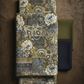 Carpet Bag Romance Blue Carpet fabric by Jason Yenter for In The Beginning Fabrics folded on a dark wood surface – large-scale antique carpet patchwork with oversized ivory roses, ornate paisley medallions, and scrollwork in charcoal, olive green, gold, and cream, perfect for vintage and statement quilt projects, 100% cotton, 3 yard cut