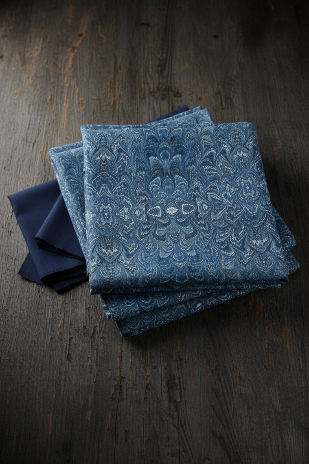 Carpet Bag Romance Blue Marble fabric by Jason Yenter for In The Beginning Fabrics folded on a dark linen surface – intricate symmetrical marbled damask with kaleidoscopic feathered medallion pattern in deep steel blue, slate, and navy with shimmering white highlights, perfect for vintage and antique-inspired quilt projects, 100% cotton, 3 yard cut