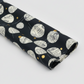 Celestial News Dropping Onyx by Zen Chic for Moda Fabrics — bold black cotton with cream newspaper circles and gold dots, folded in a diagonal sweep showing fabric drape and body. 