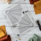 Creative Grids Non-Slip Circle Savvy Ruler on a white wood surface surrounded by folded quilting fabrics in cream, rust, mustard, and sage, with colorful wonder clips and a rotary cutter