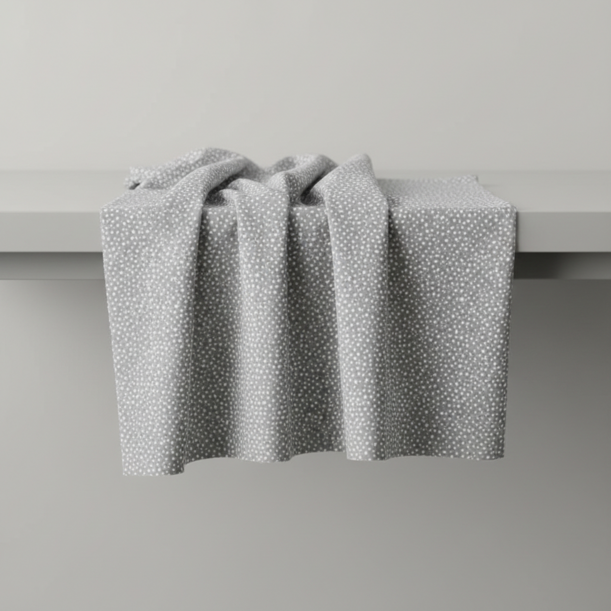 Essentials Connect The Dots Gray quilting cotton by Susan Winget for Wilmington Prints — fabric draped over a grey surface showing natural folds and raw cut edge, warm grey ground with tossed soft white scattered dots
