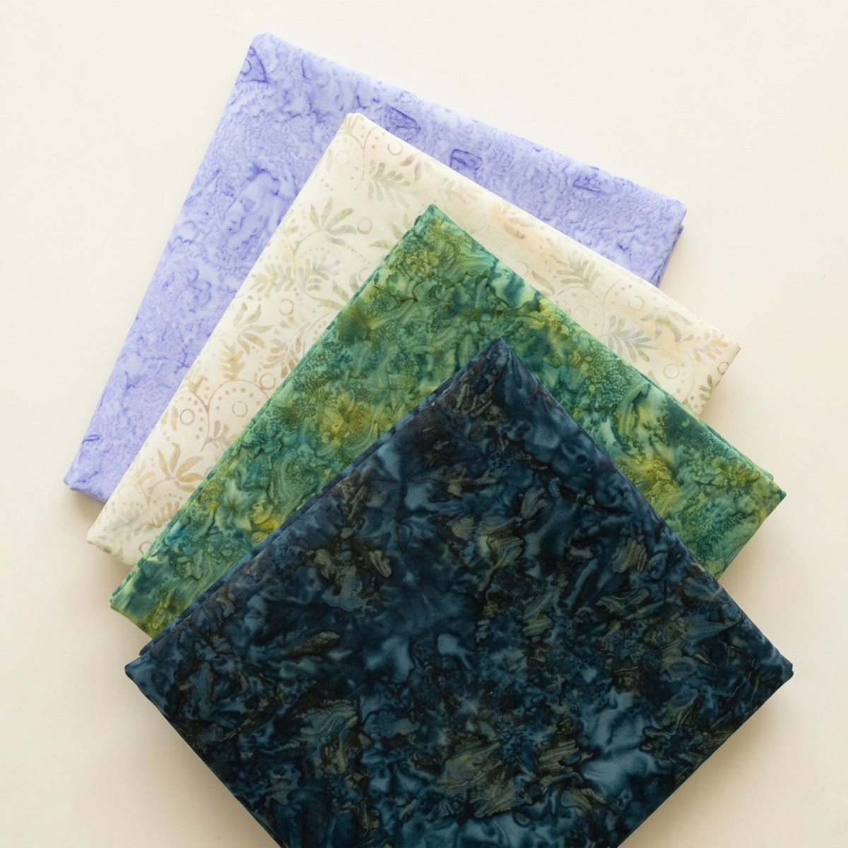 Four folded Riley Blake Designs fabrics arranged in a fan: Color Play Mottled Rainstorm, Expressions Batiks Amazon, Breathe Laurel, and Periwinkle, in dark teal, green, cream, and lavender.
