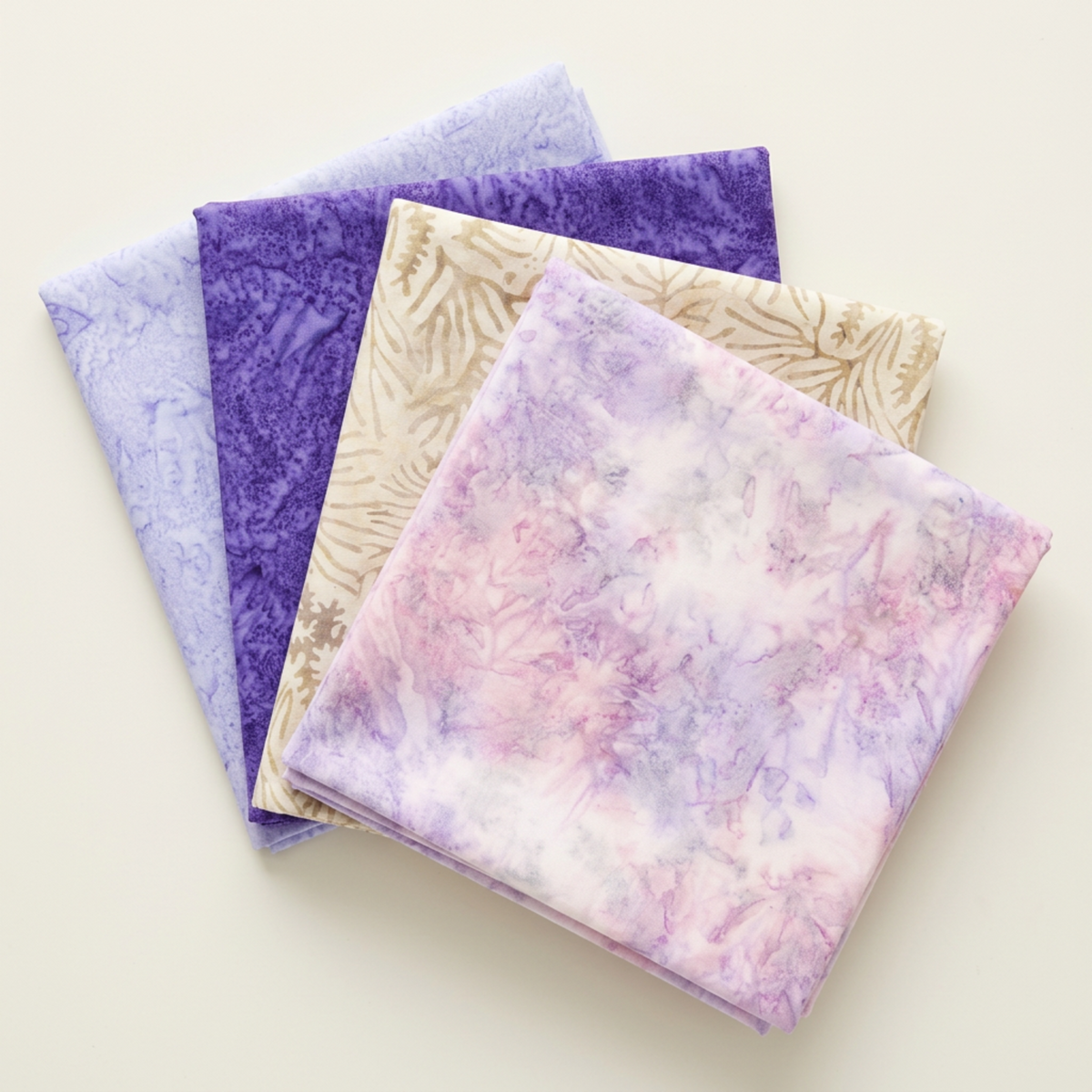 Four folded Riley Blake Designs fabrics arranged in a fan: Color Play Mottled Lilac Lustre, Expressions Batiks Breathe Ecru, Purple II, and Periwinkle.