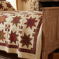 Scraps of Kindness Cream Nine Patch Boxes quilting cotton by Kim Diehl for Henry Glass — traditional quilt in a cozy cottage room, cream cross-grid background with dark brown, burgundy, red, and olive folk-art blocks, dense hand quilting