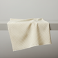 Scraps of Kindness Cream Nine Patch Boxes quilting cotton by Kim Diehl for Henry Glass — fabric draped over a grey surface showing natural folds and raw cut edge, warm cream ground with evenly spaced tiny dark brown four-point cross clusters