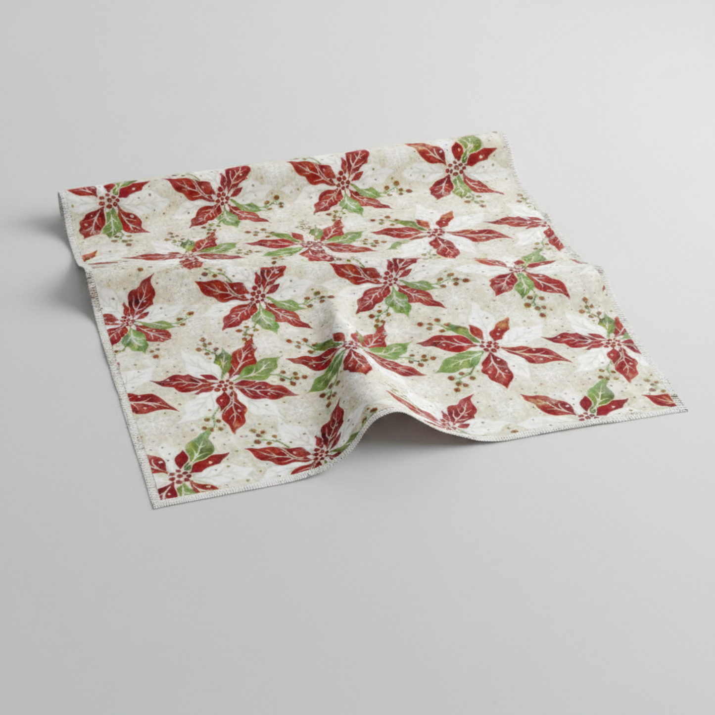 Winter Solstice II Cream Poinsettia Metallic quilting cotton by Jason Yenter for In The Beginning Fabrics — fabric draped over a grey surface showing natural folds and raw cut edge, kaleidoscopic watercolor poinsettias in red, white, and green with gold metallic berry sprigs on warm cream ground. Coordinating fabrics and quilt patterns are available at IraRobi Quilts.