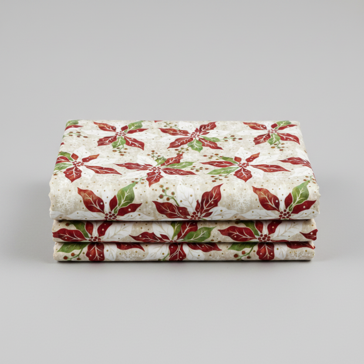 Winter Solstice II Cream Poinsettia Metallic quilting cotton by Jason Yenter for In The Beginning Fabrics — three folded yards stacked on a grey surface showing kaleidoscopic watercolor poinsettias in red, white, and green with gold metallic berry sprigs on warm cream and ecru ground. Coordinating fabrics and quilt patterns are available at IraRobi Quilts.