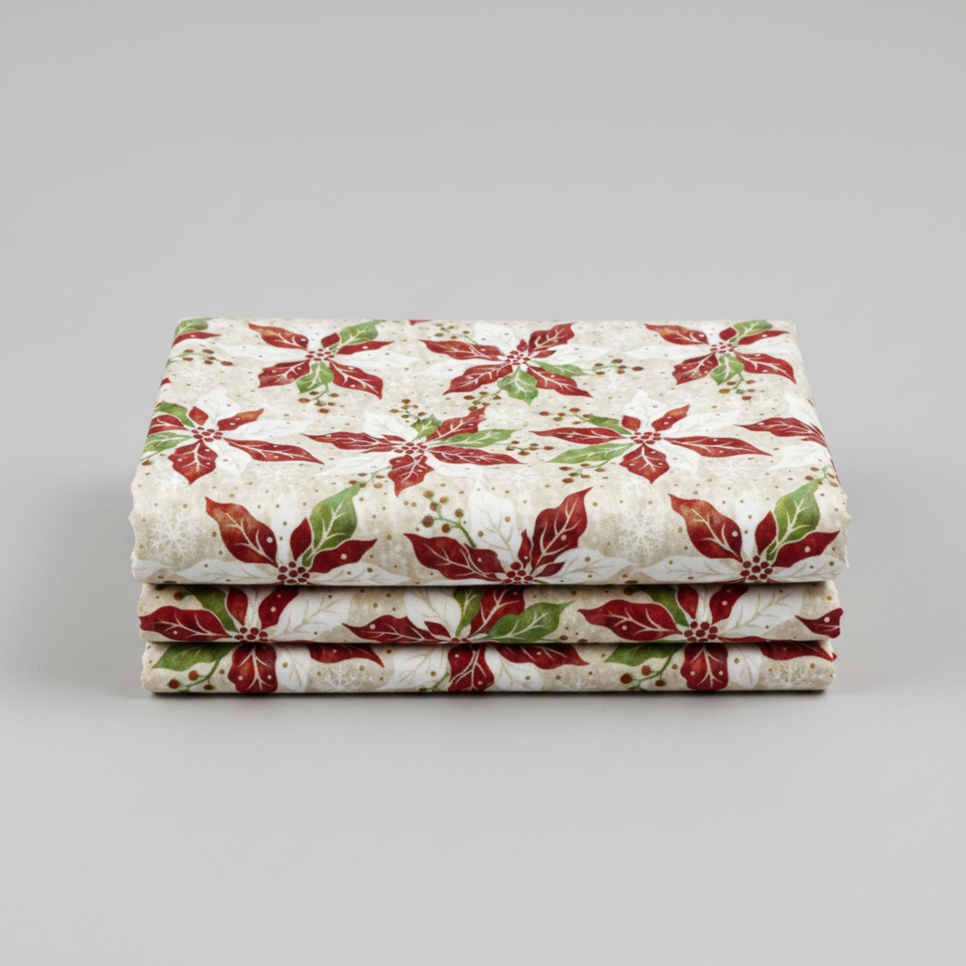 Winter Solstice II Cream Poinsettia Metallic quilting cotton by Jason Yenter for In The Beginning Fabrics — three folded yards stacked on a grey surface showing kaleidoscopic watercolor poinsettias in red, white, and green with gold metallic berry sprigs on warm cream and ecru ground. Coordinating fabrics and quilt patterns are available at IraRobi Quilts.