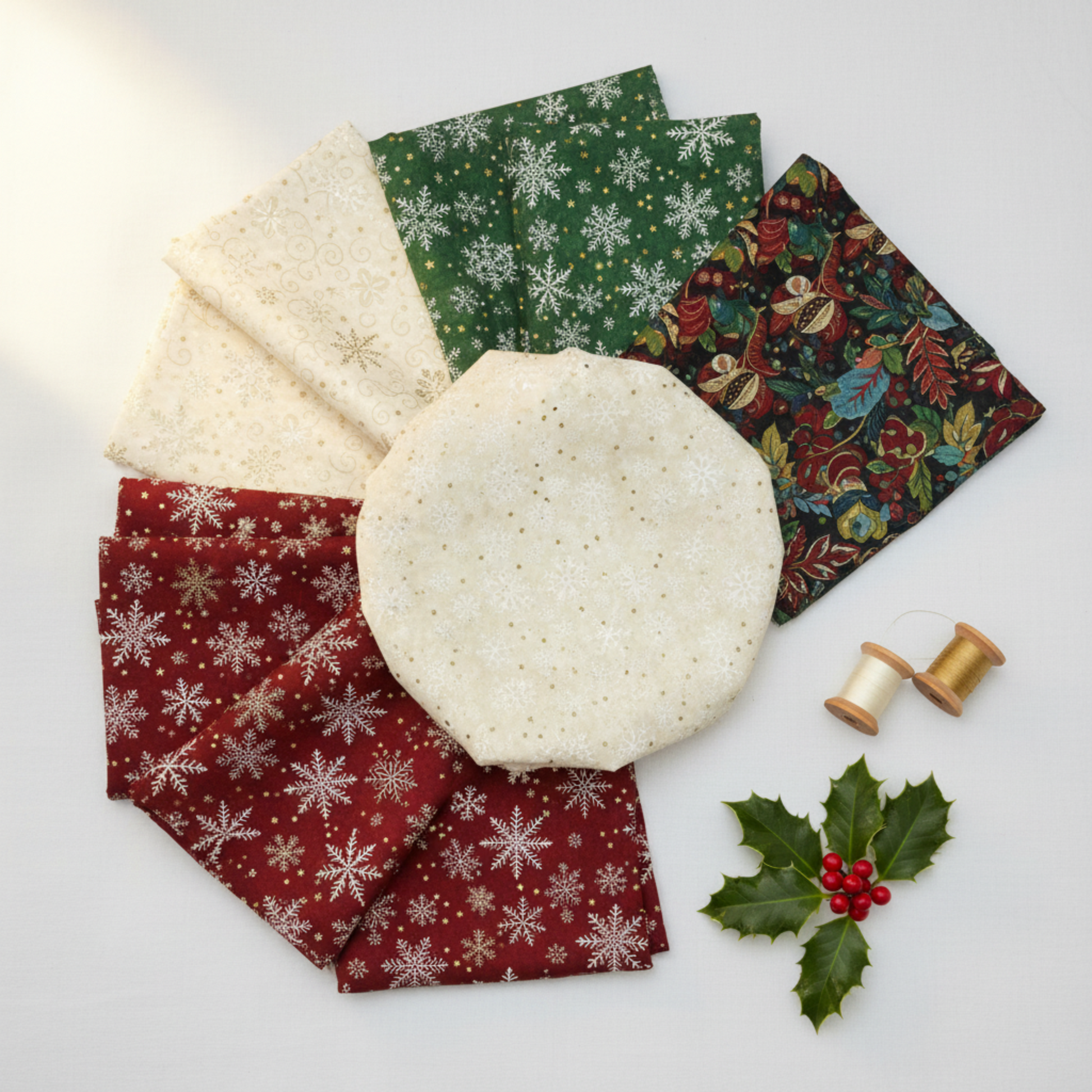 Winter Solstice II Cream Snowflakes Metallic Fabric by Jason Yenter for In The Beginning Fabrics — shown with coordinating quilting cottons fanned flat, with cream and gold metallic thread spools and a holly sprig. Coordinating fabrics and quilt patterns are available at IraRobi Quilts.