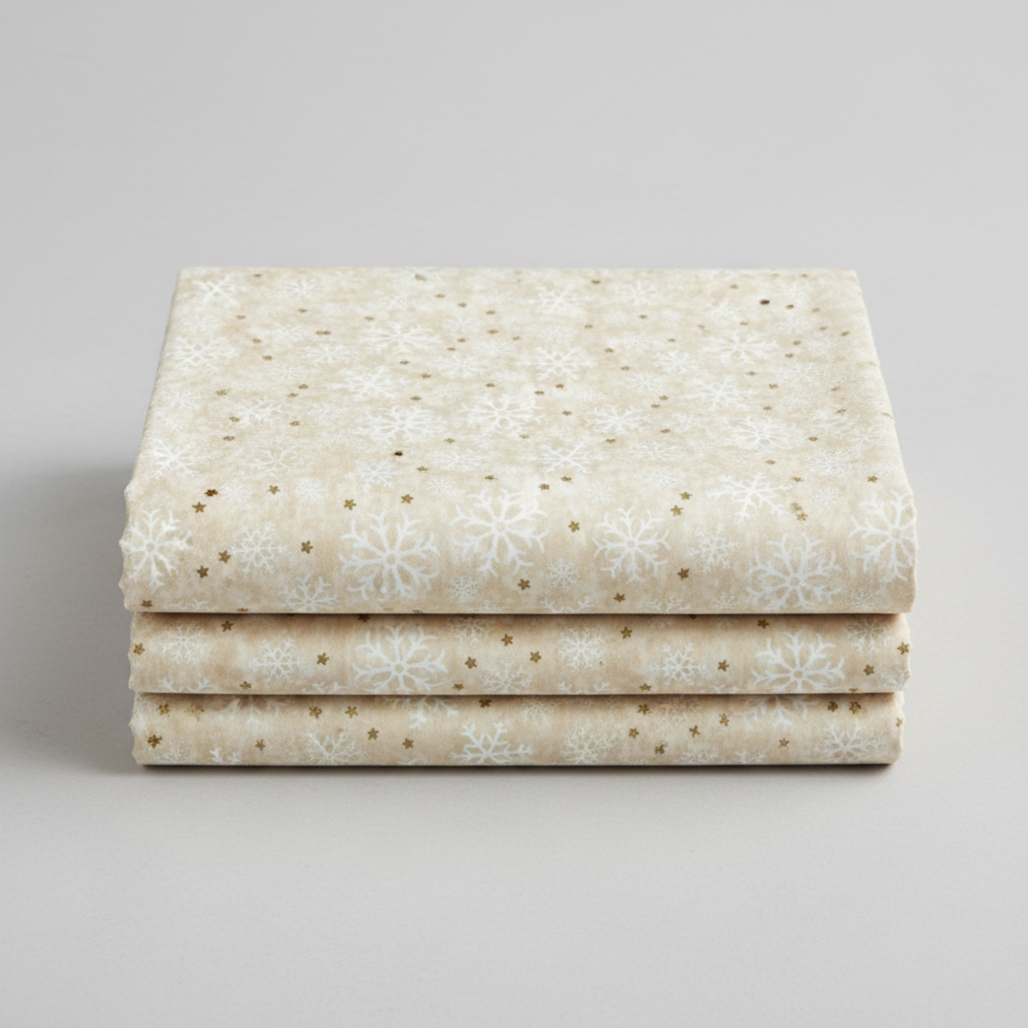 Winter Solstice II Cream Snowflakes Metallic quilting cotton by Jason Yenter for In The Beginning Fabrics — three folded yards stacked on a grey surface showing tossed white snowflakes with gold metallic star dots on warm mottled ecru and cream ground. Quilt blocks shown for inspiration. Coordinating fabrics and quilt patterns are available at IraRobi Quilts.