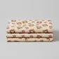 The Fox Homestead Cream Square Wreath quilting cotton folded in a neat stack — warm cream ground with tossed square daisy wreath clusters in dusty rose, muted burgundy, and olive-khaki by Stacy West for Henry Glass