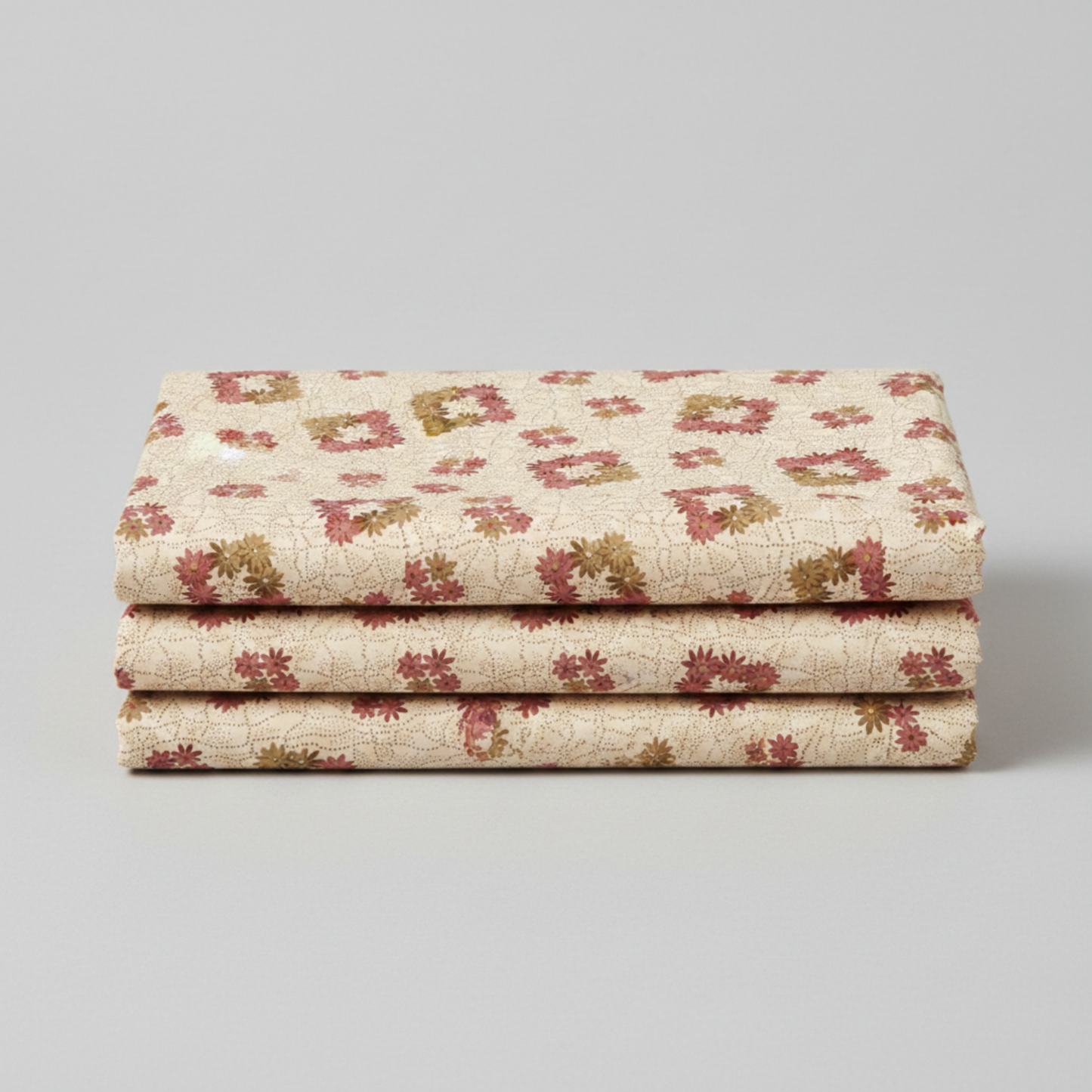 The Fox Homestead Cream Square Wreath quilting cotton folded in a neat stack — warm cream ground with tossed square daisy wreath clusters in dusty rose, muted burgundy, and olive-khaki by Stacy West for Henry Glass