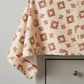 The Fox Homestead Cream Square Wreath quilting cotton draped over a light grey table edge — warm cream with tossed daisy clusters in dusty rose, muted burgundy, and olive-khaki, raw cut edges, by Stacy West for Henry Glass