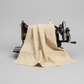 The Fox Homestead Cream Swirl Floral Texture quilting cotton draped over a vintage sewing machine — warm sand with tiny white paisley swirls and brown dots, raw cut edges, by Stacy West for Henry Glass