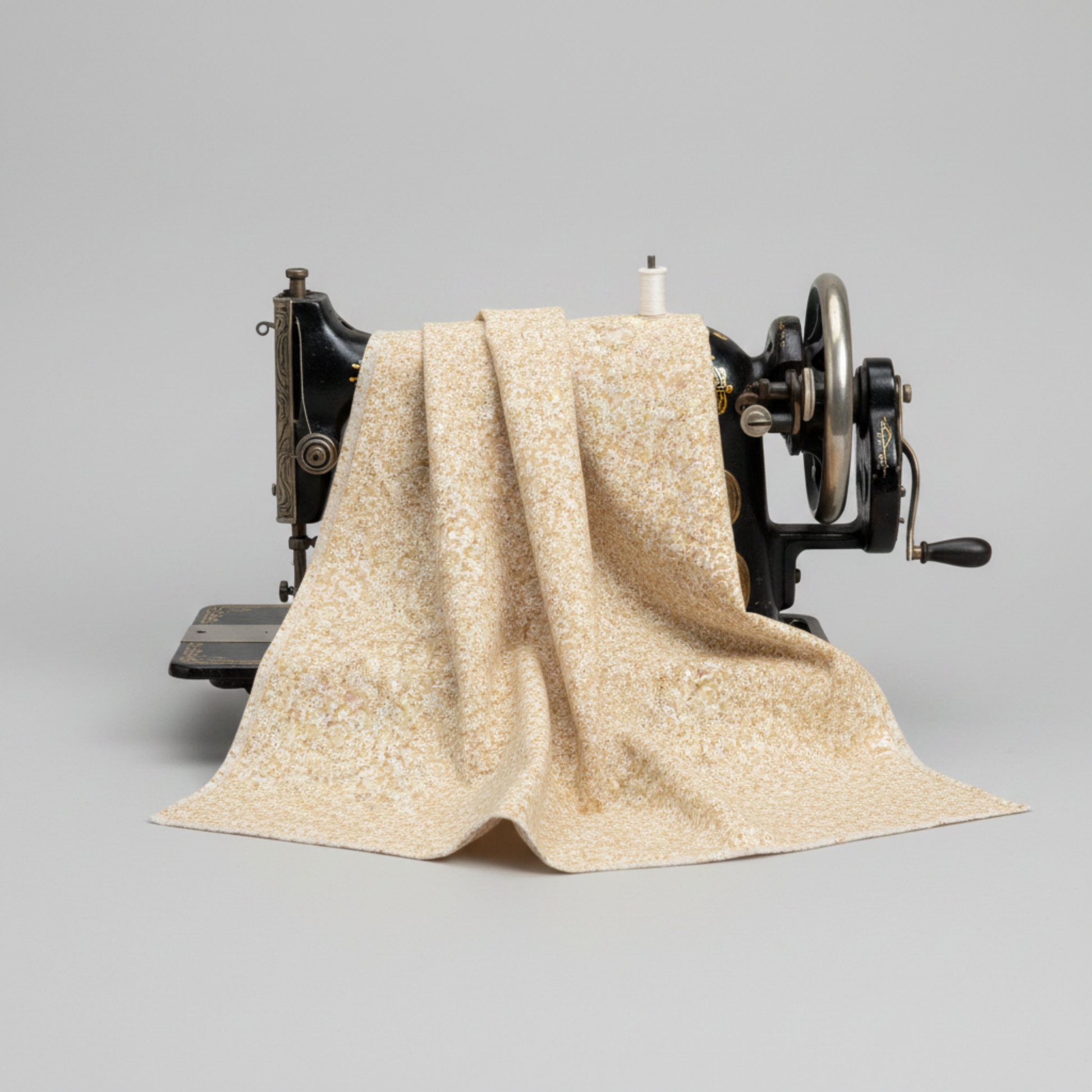 The Fox Homestead Cream Swirl Floral Texture quilting cotton draped over a vintage sewing machine — warm sand with tiny white paisley swirls and brown dots, raw cut edges, by Stacy West for Henry Glass